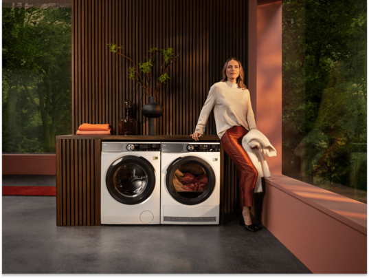 Woman standing next to washing machine and dryer unit..